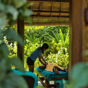 Seorang tamu menikmati pijat relaksasi di area spa terbuka yang dikelilingi taman tropis di Waterbom Bali, menciptakan suasana tenang dan menyegarkan.