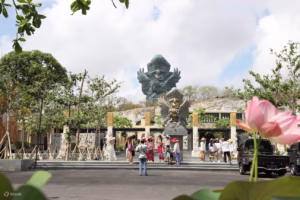 Pengunjung berkumpul di area depan Garuda Wisnu Kencana Bali dengan latar patung Garuda dan taman terbuka, menciptakan suasana teater jalanan yang hidup dan artistik.