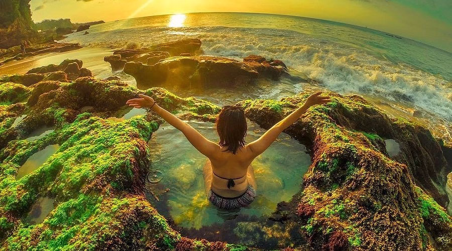 Wisatawan menikmati kolam alami di antara karang saat sunset di Pantai Tegal Wangi Bali