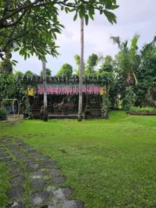 Area kafe outdoor di Big Garden Corner Bali dengan taman hijau luas, ayunan anak, dan dekorasi bunga gantung yang asri dan Instagramable.