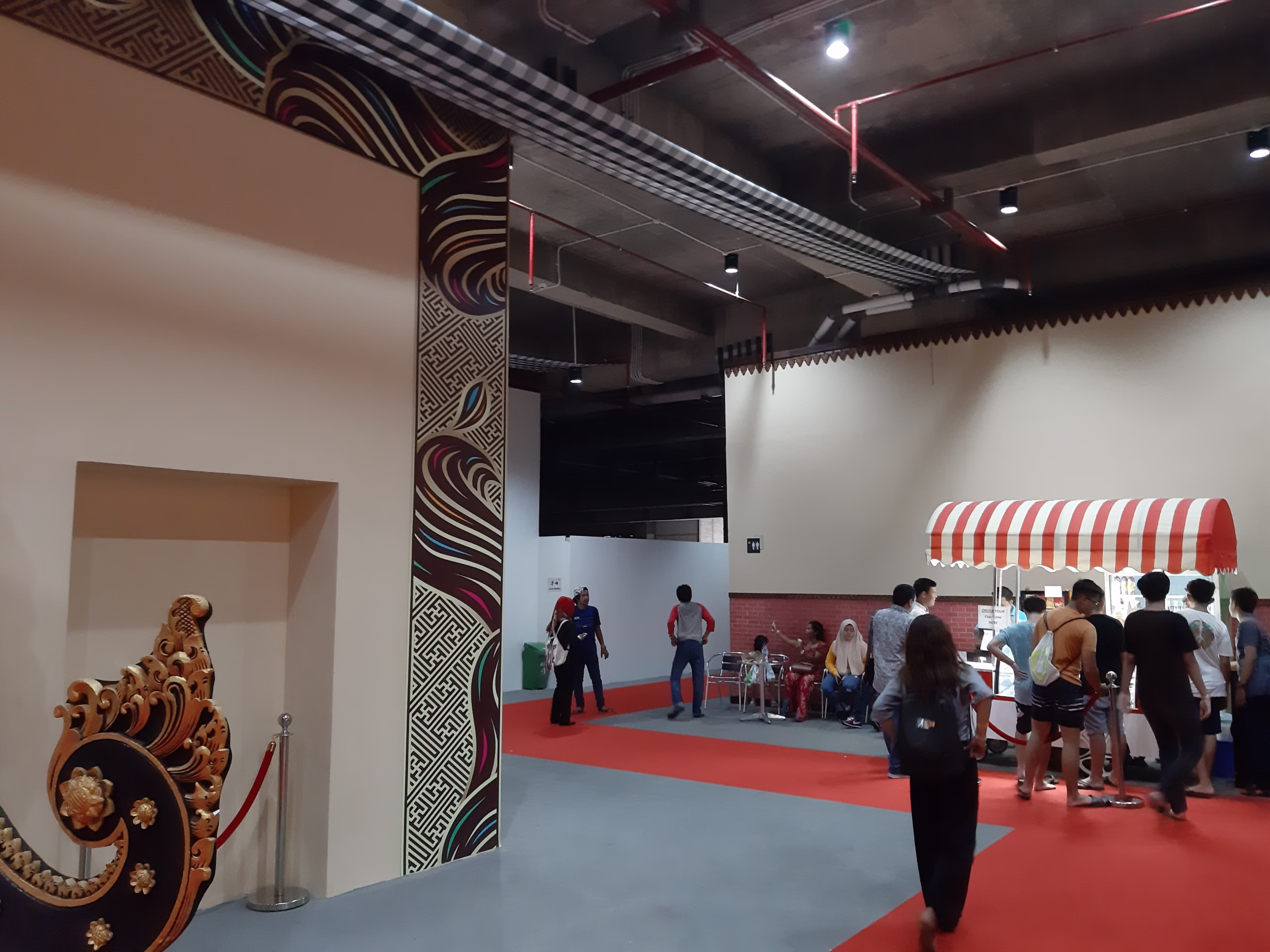 Suasana dalam ruangan Garuda Wisnu Kencana yang menampilkan ornamen tradisional Bali dan stan kuliner, dikunjungi oleh wisatawan untuk bersantai dan menikmati makanan. 