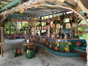 Area kuliner dengan desain tropis warna-warni di Waterbom Bali, menampilkan bar makanan dan minuman yang artistik dengan dekorasi alami dan tempat duduk santai.