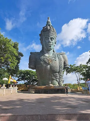 Patung Dewa Wisnu di Plaza Wisnu, Garuda Wisnu Kencana Bali, berdiri megah dikelilingi pepohonan dan langit cerah sebagai simbol pelindung alam semesta.
