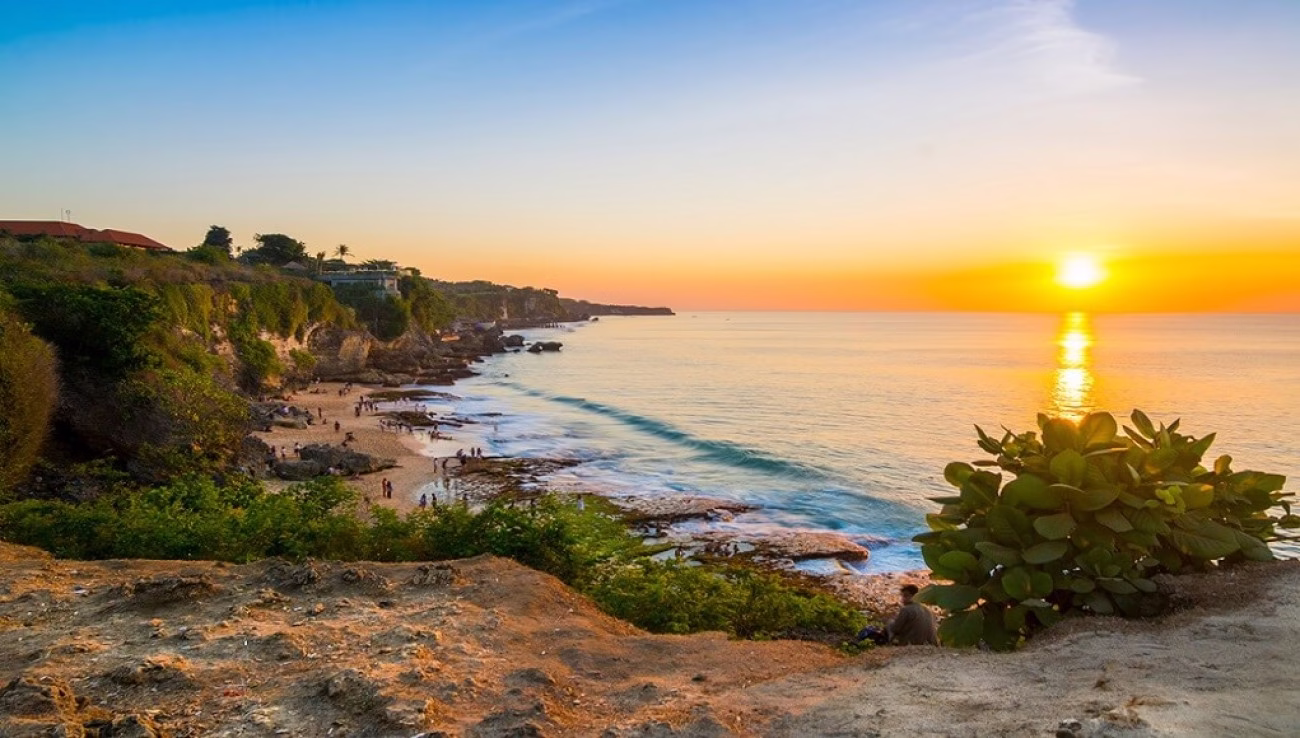 Matahari terbenam di ufuk barat Tegal Wangi Beach, menciptakan siluet tebing dan suasana damai