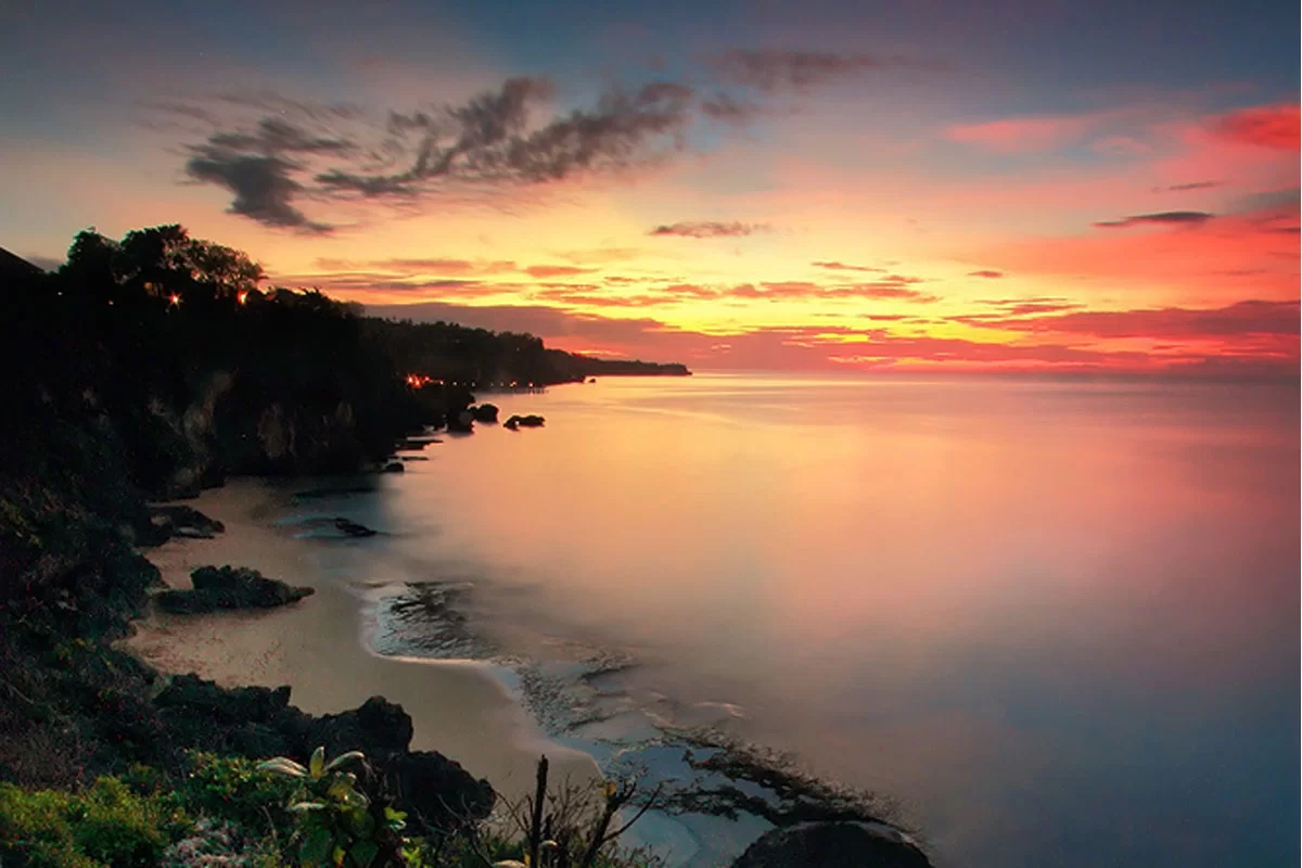 Matahari terbenam di ufuk barat Tegal Wangi Beach, menciptakan siluet tebing dan suasana damai