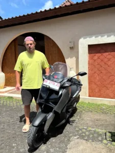 Wisatawan asing berdiri di samping motor matic dari layanan sewa motor Bali, siap digunakan untuk rental selama liburan.
